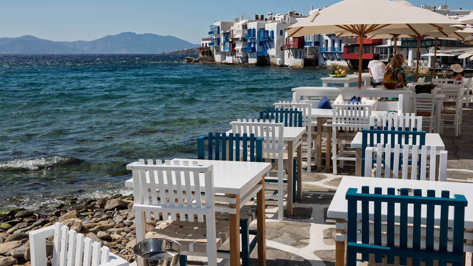 Mesas de restaurante à beira-mar em Mykonos, com cadeiras brancas e azuis