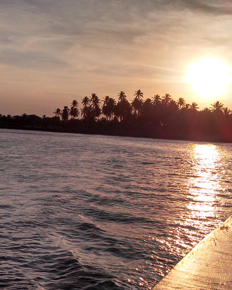 Sol baixo refletindo na água da Lagoa Mundaú, visto de dentro de um barco