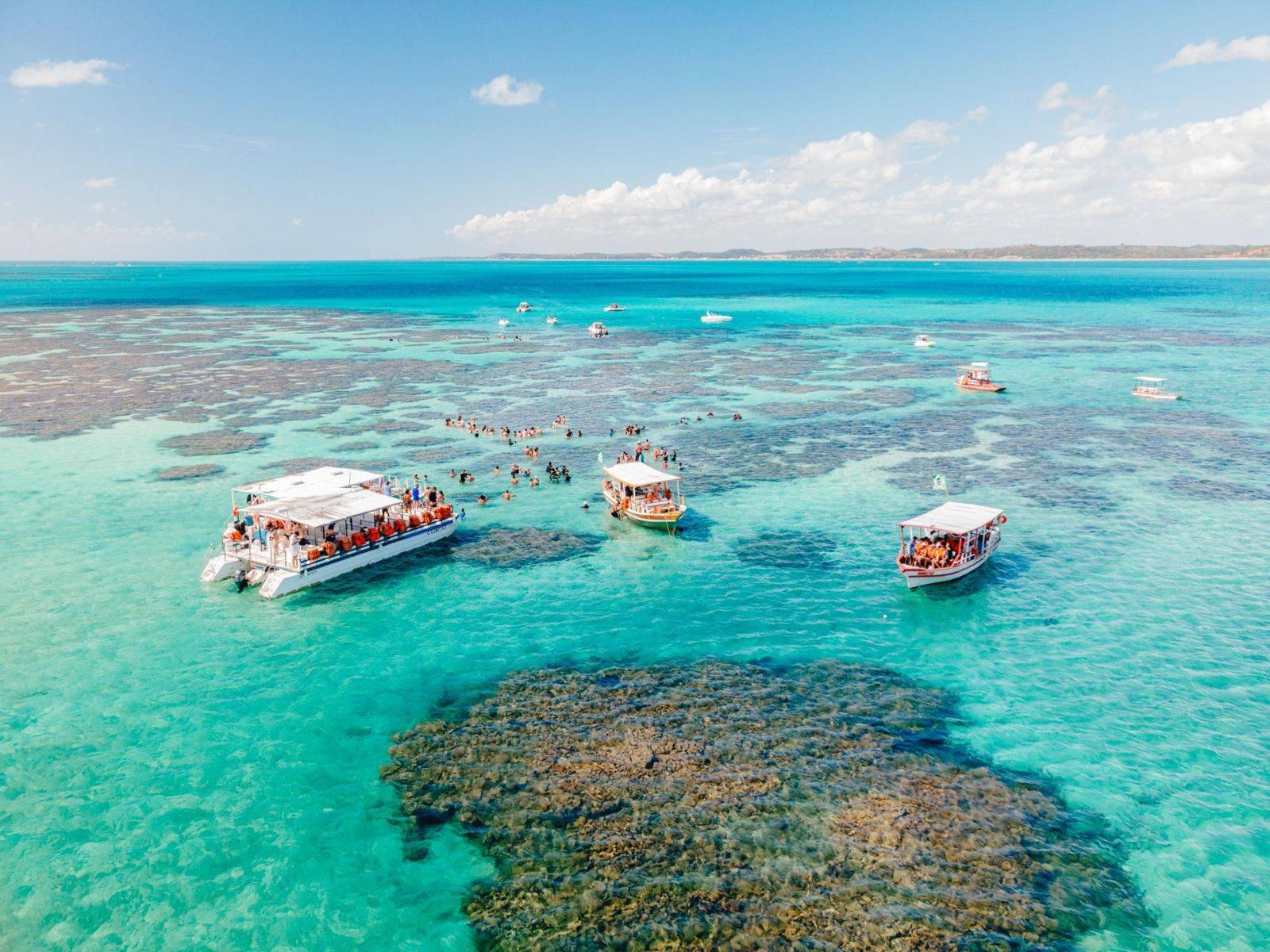 Vista aérea das piscinas naturais de Maragogi com barcos entre os recifes