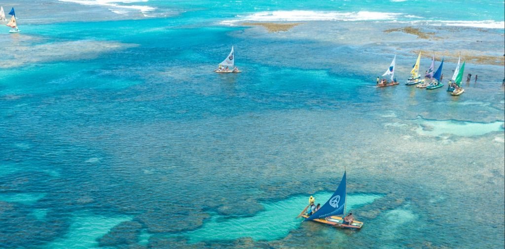 Vista aérea de jangadas com velas coloridas sobre as piscinas naturais de Porto de Galinhas