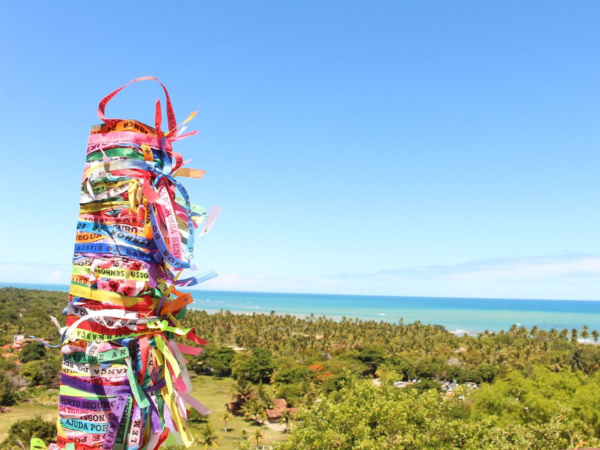 Poste coberto de fitinhas coloridas em Arraial d'Ajuda, com o coqueiral e o mar ao fundo