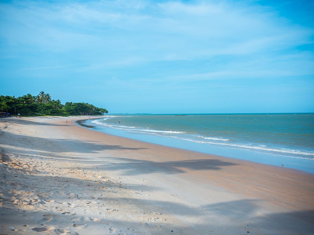 Praia larga e quase vazia em Porto Seguro, com areia clara, mar calmo e coqueiros ao fundo