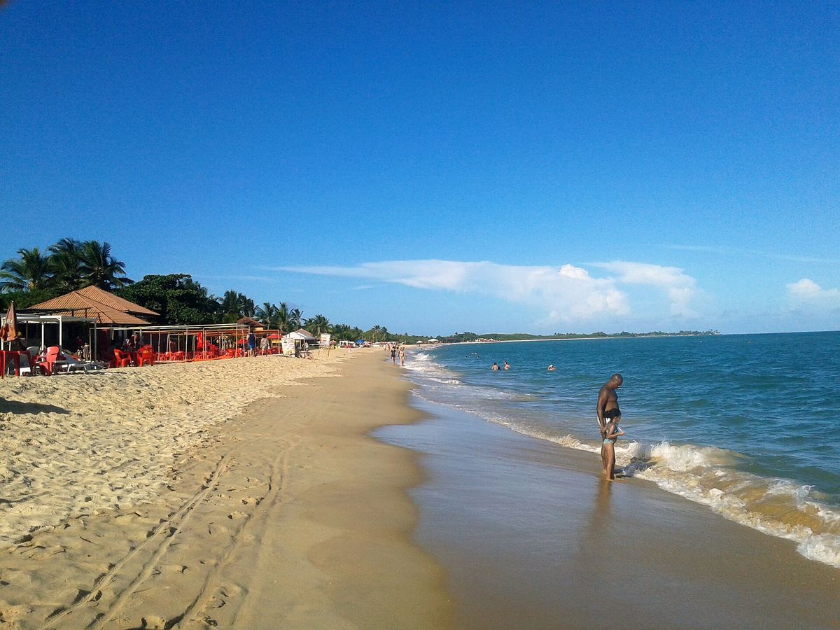 Praia de Taperapuã com barracas de praia, cadeiras vermelhas, banhistas e coqueiros
