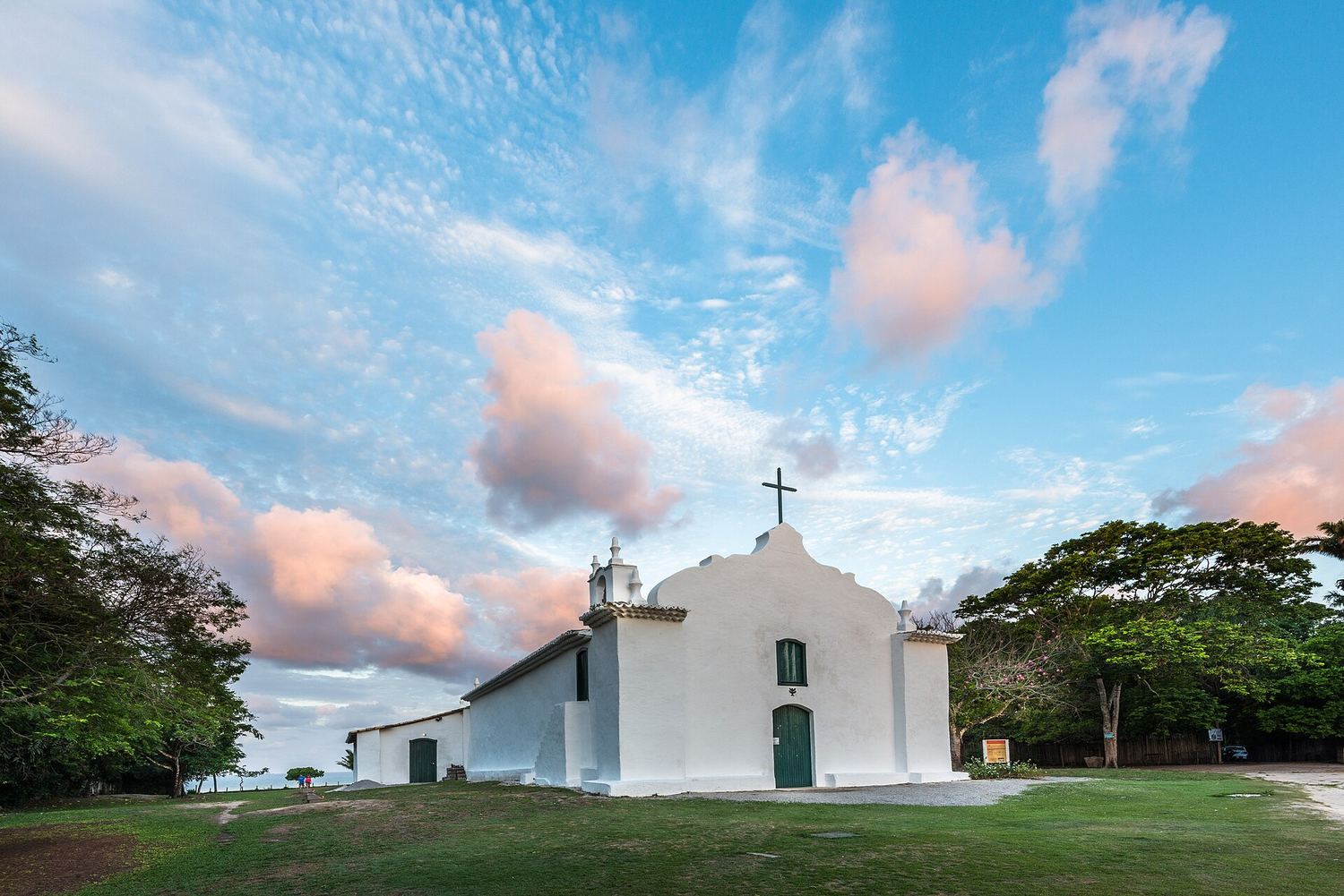 Igreja branca de São João Batista no gramado do Quadrado de Trancoso, sob um céu com nuvens rosadas
